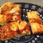 Three slices of deep-dish pizza with rich cheese and tangy tomato sauce rest on a patterned blue plate, crafted with a robust sourdough pizza dough for an irresistible twist.