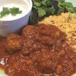 Moroccan meatballs on a plate with couscous, leaves and a white dip.