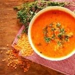 An orange coloured Lentil soup using red lentils in a bowl with some dried lentils next to the bowl.