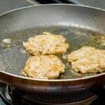 Pork burgers frying in a frying pan with oil.
