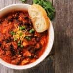 turkey mince chilli in a white bowl with garlic bread on the side