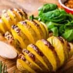 hasselback potatoes on a wooden board with salad.