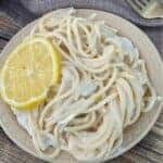 Plate of lemon spaghetti topped with a slice of lemon.