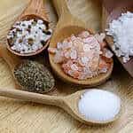 Image of different salts in wooden spoons on a wooden table