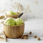 An image of pistachio ice cream in a wooden bowl on white background