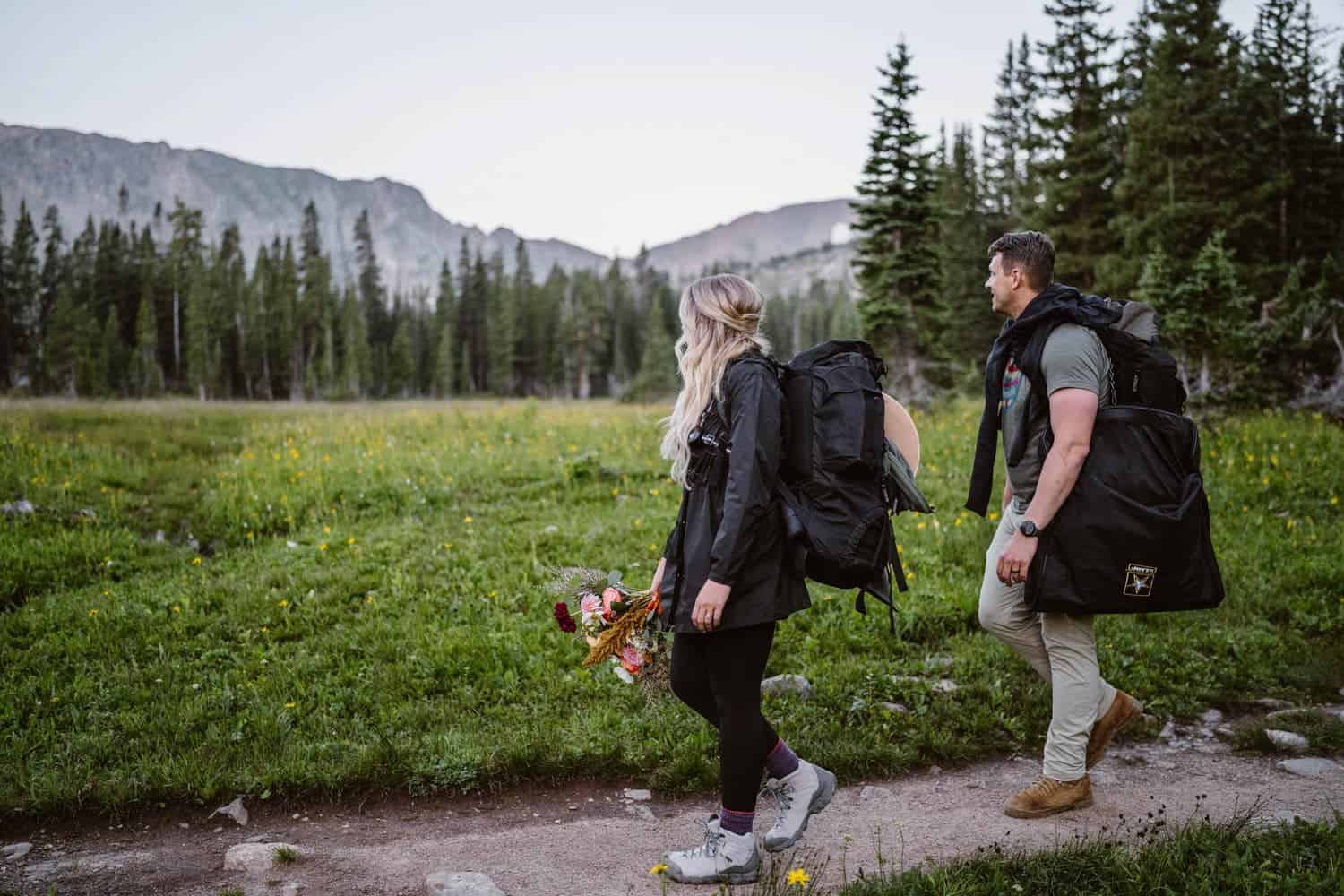 Bride and groom hiking with their wedding gear in the mountains.