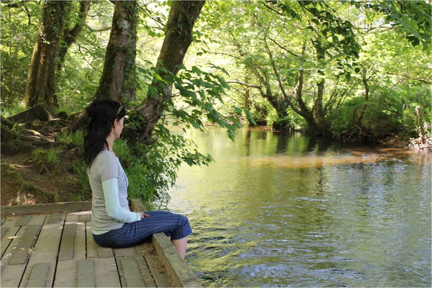 a woman with good posture, practising mindfulness sitting on a riverbank