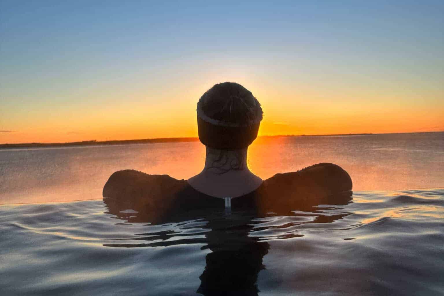 A woman in a dark swimsuit and headband relaxing in a hot spring pool at sunset. Adding in time to relax helps avoid overload and burnout when travelling with ADHD.