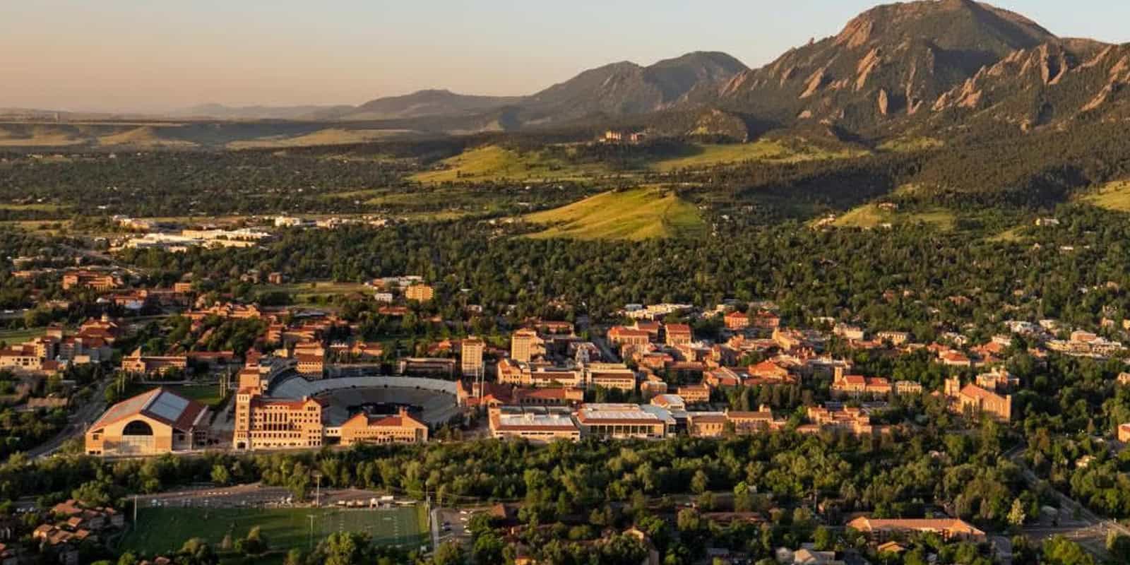 Aerial view of the University of Colorado Boulder campus with surrounding mountains, showcasing the integration of academic buildings and green spaces, highlighting the university's commitment to centralized operations and efficient conference management with Kinetic Software.