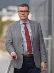 Prelegent na PHD RISK Summerschool, konferencji o ryzyku i zarządzaniu, w profesjonalnym stroju, na tle miasta.