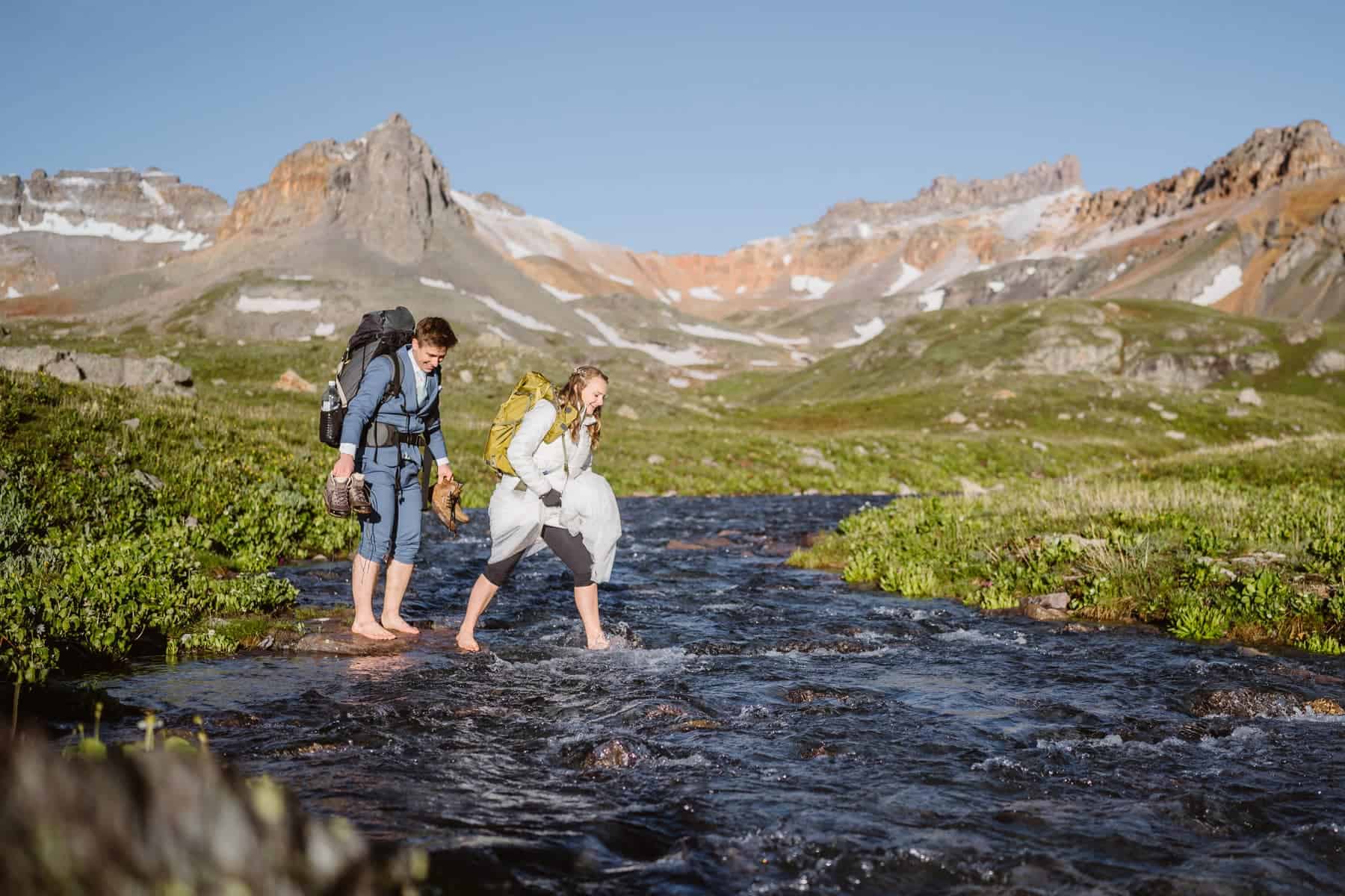 A couple crossing a stream in their elopement attire.