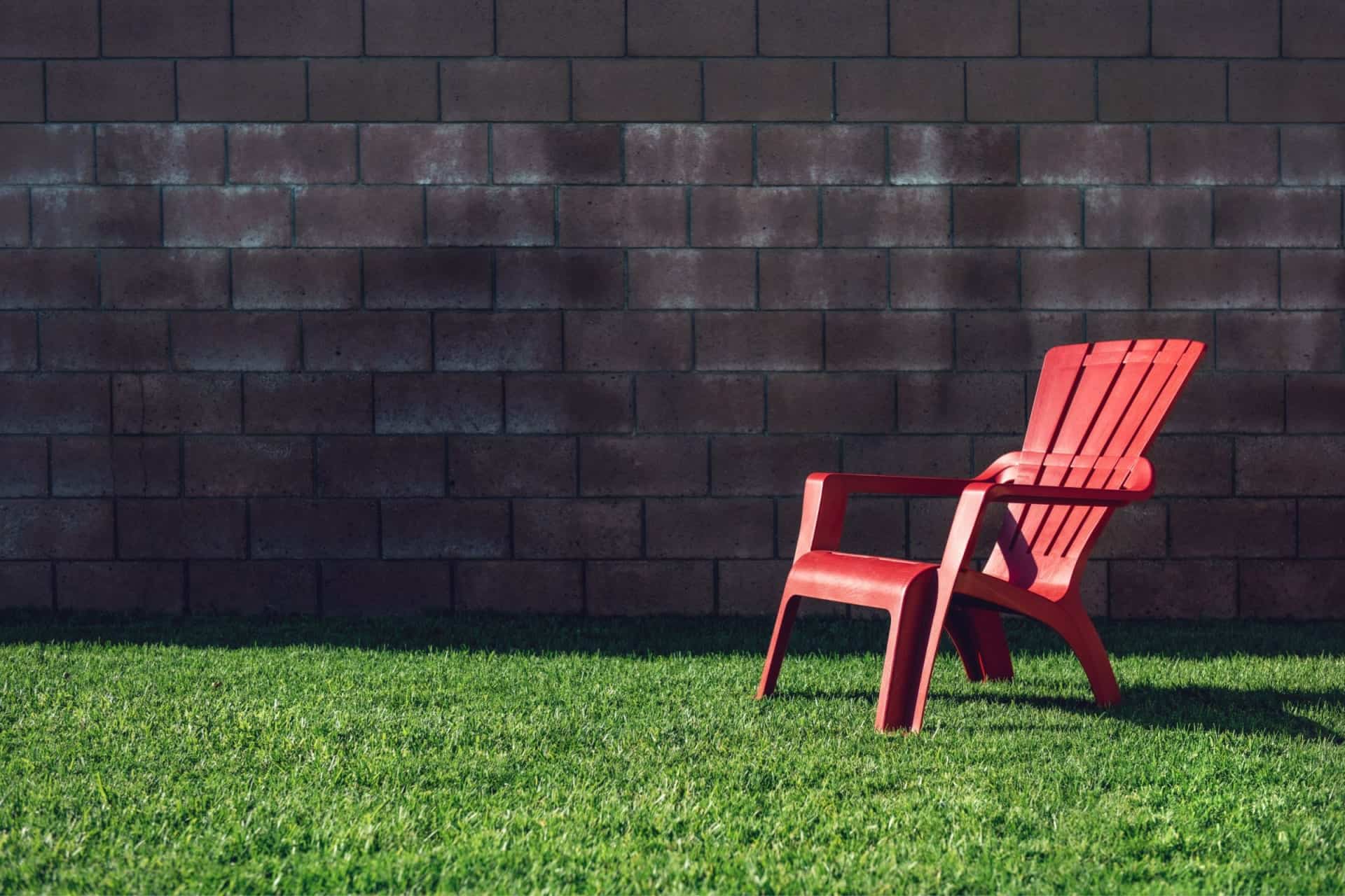 A red adirondack chair provides respite on the grass in front of a brick wall.