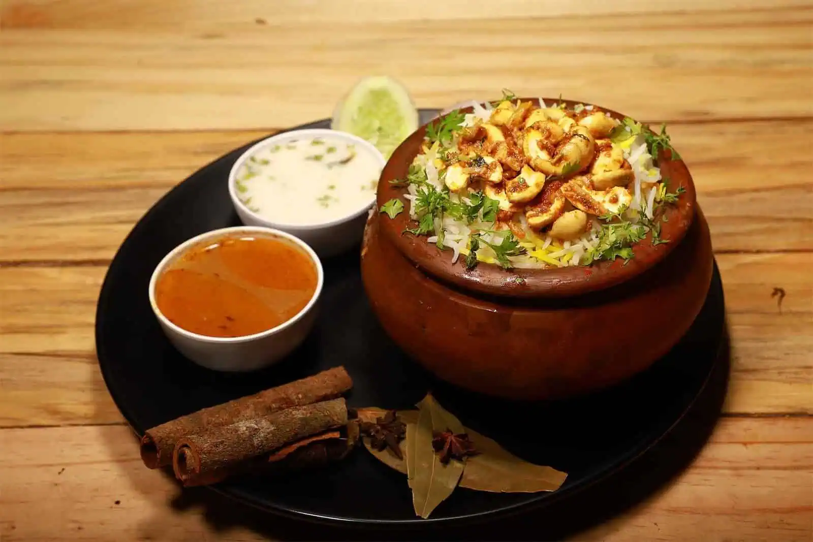 Freshly prepared Hyderabadi biryani served in a traditional clay pot with side raita, spicy curry, and aromatic spices, highlighting authentic Indian flavors at Biryani Place.