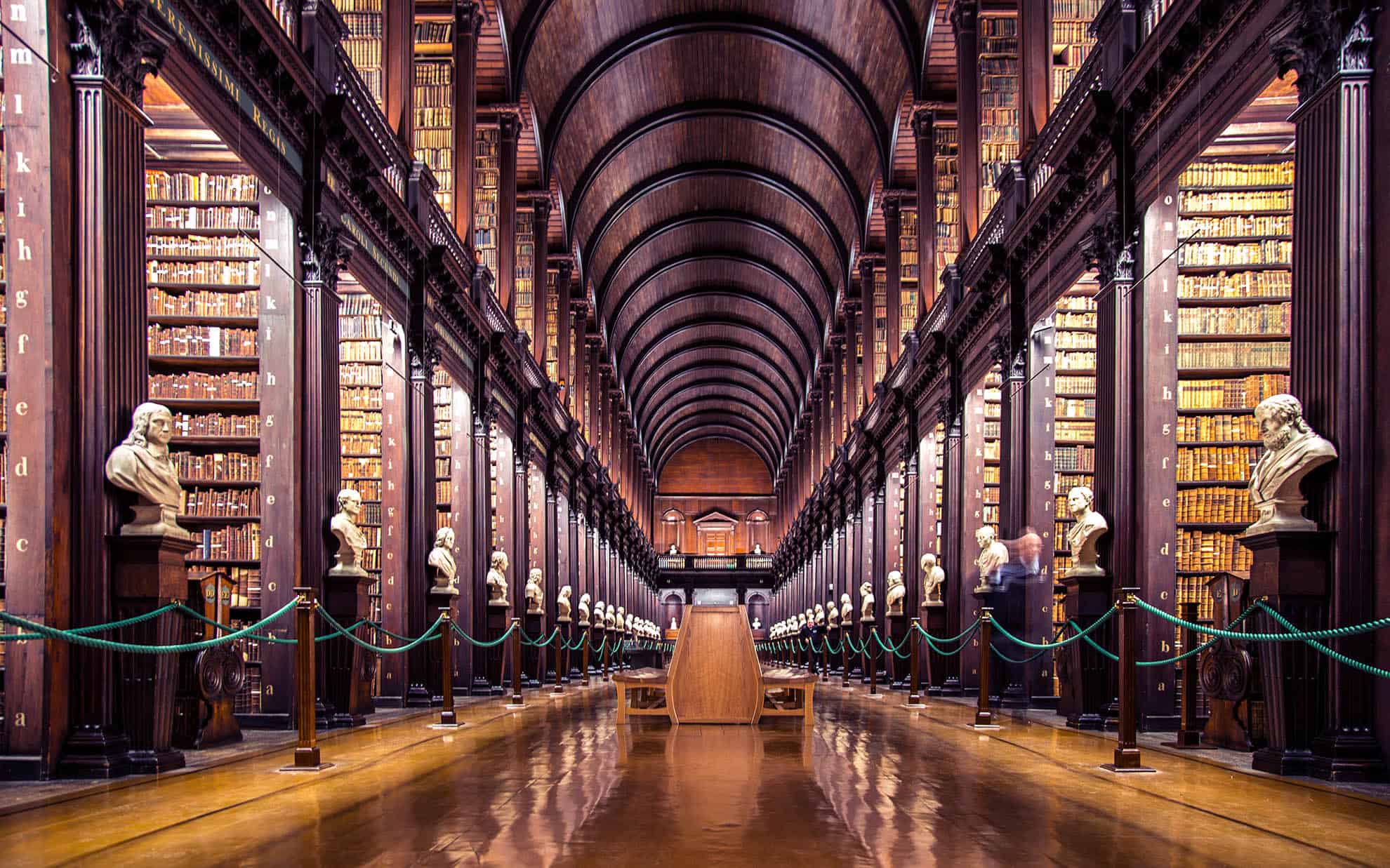 The breathtaking Long Room Library at Trinity College, with towering wooden bookshelves filled with historic books and a polished floor reflecting the soft lighting.
