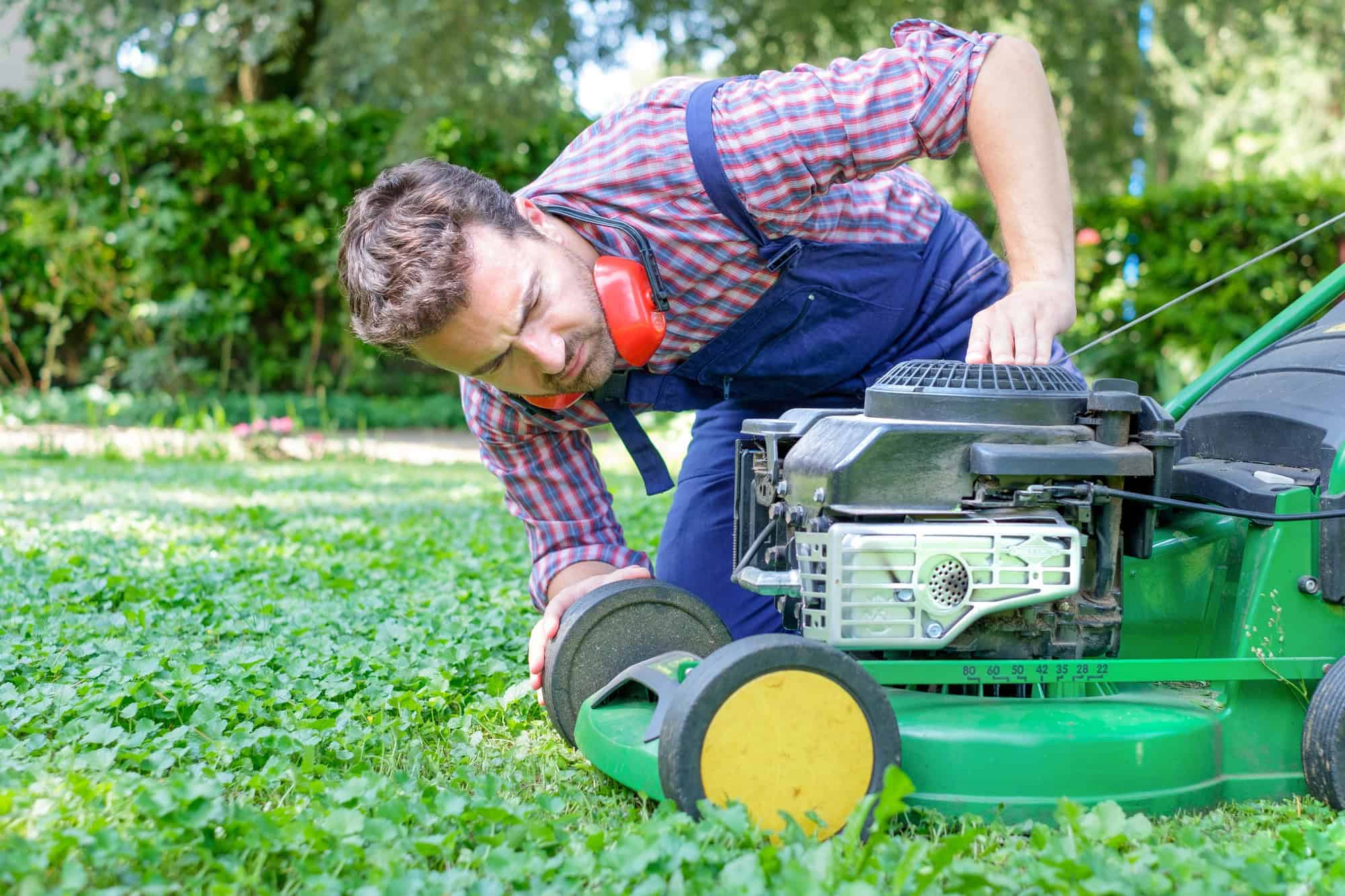 One guy portrait cutting the garden grass having problem with the lawn mower