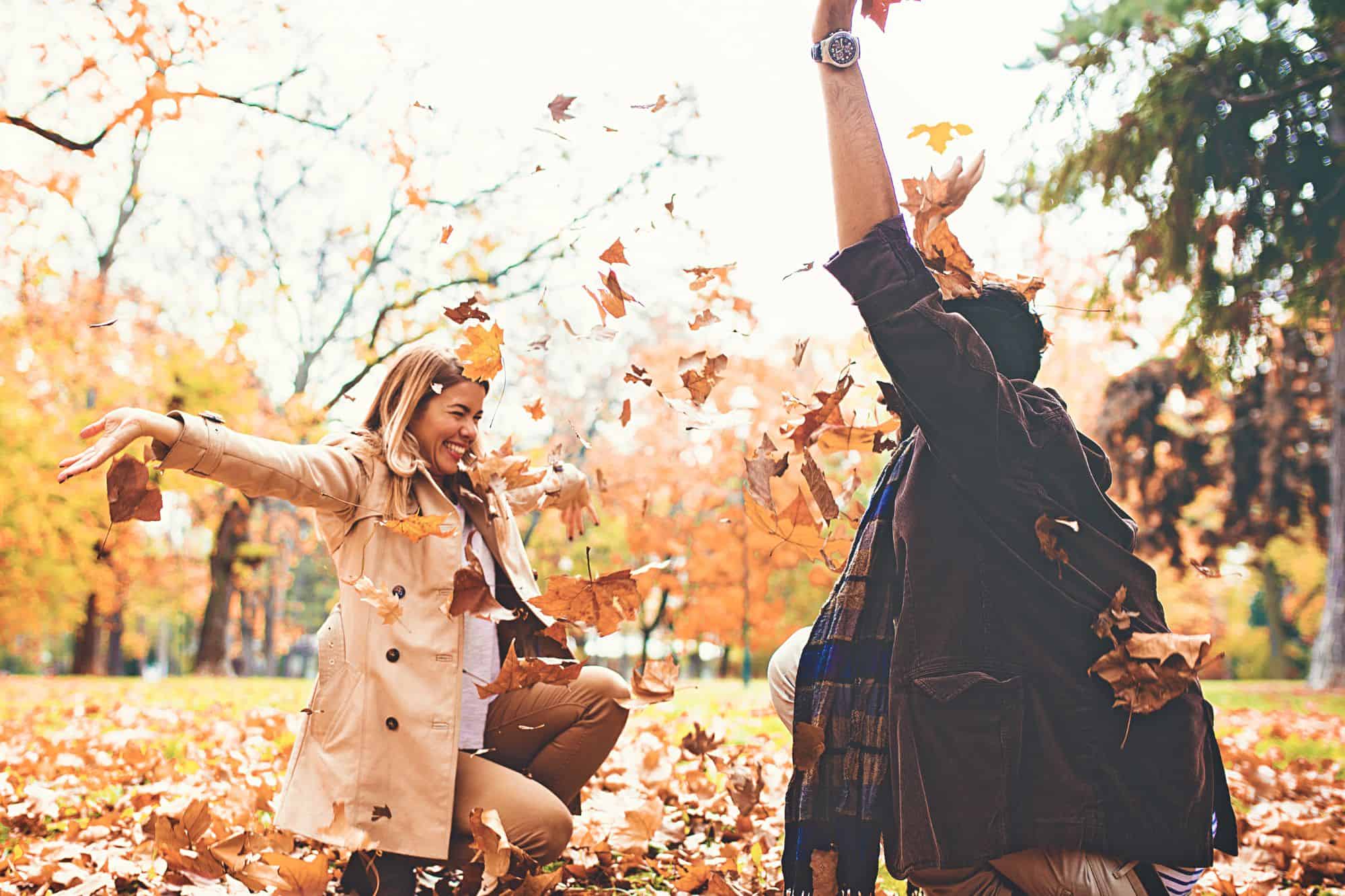 Happy couple who decided to fall back into dating, enjoying the crisp fall outdoors while throwing autumn leaves at each other.