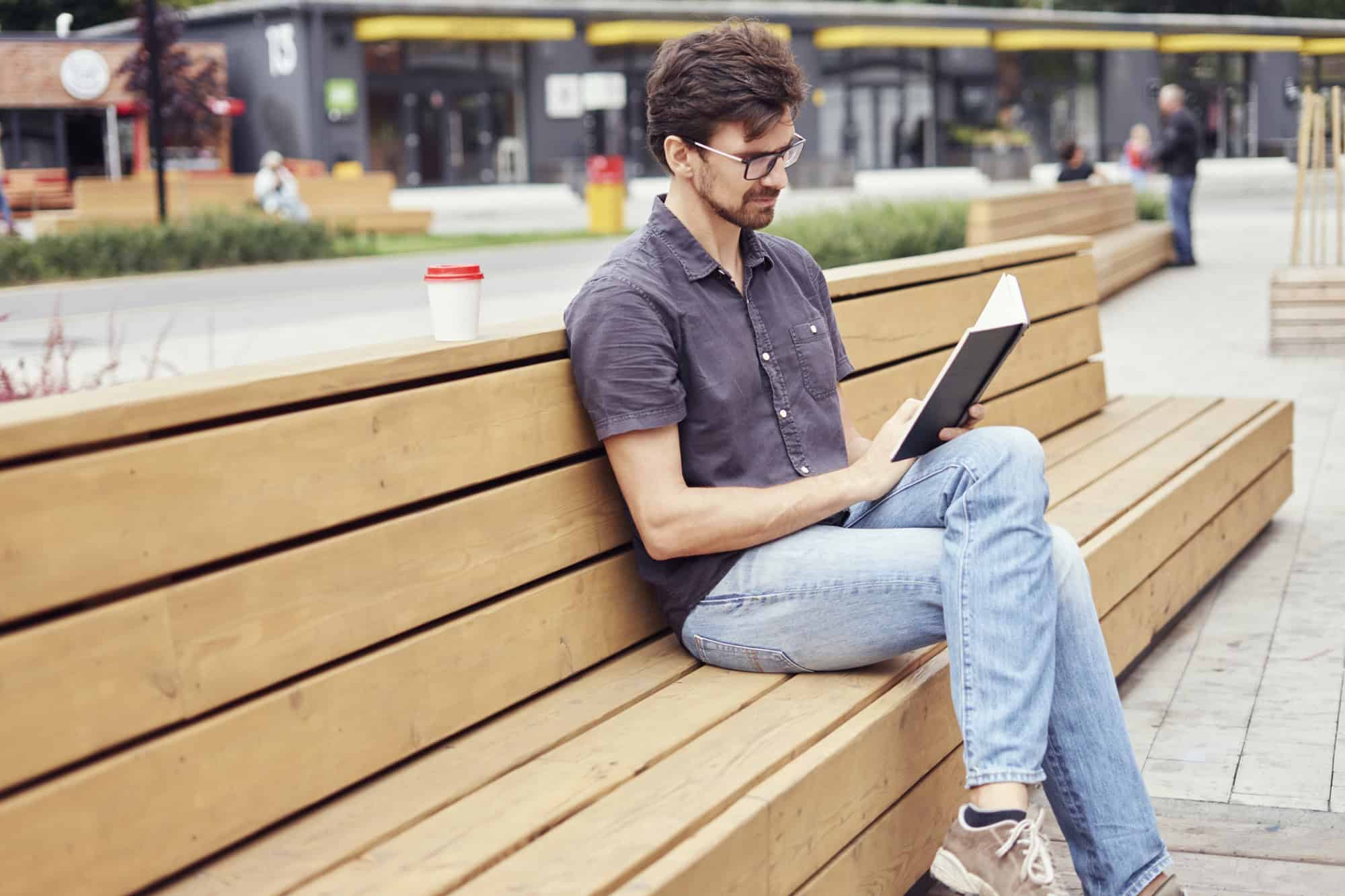 Introverted man sitting on a bench reading a book.