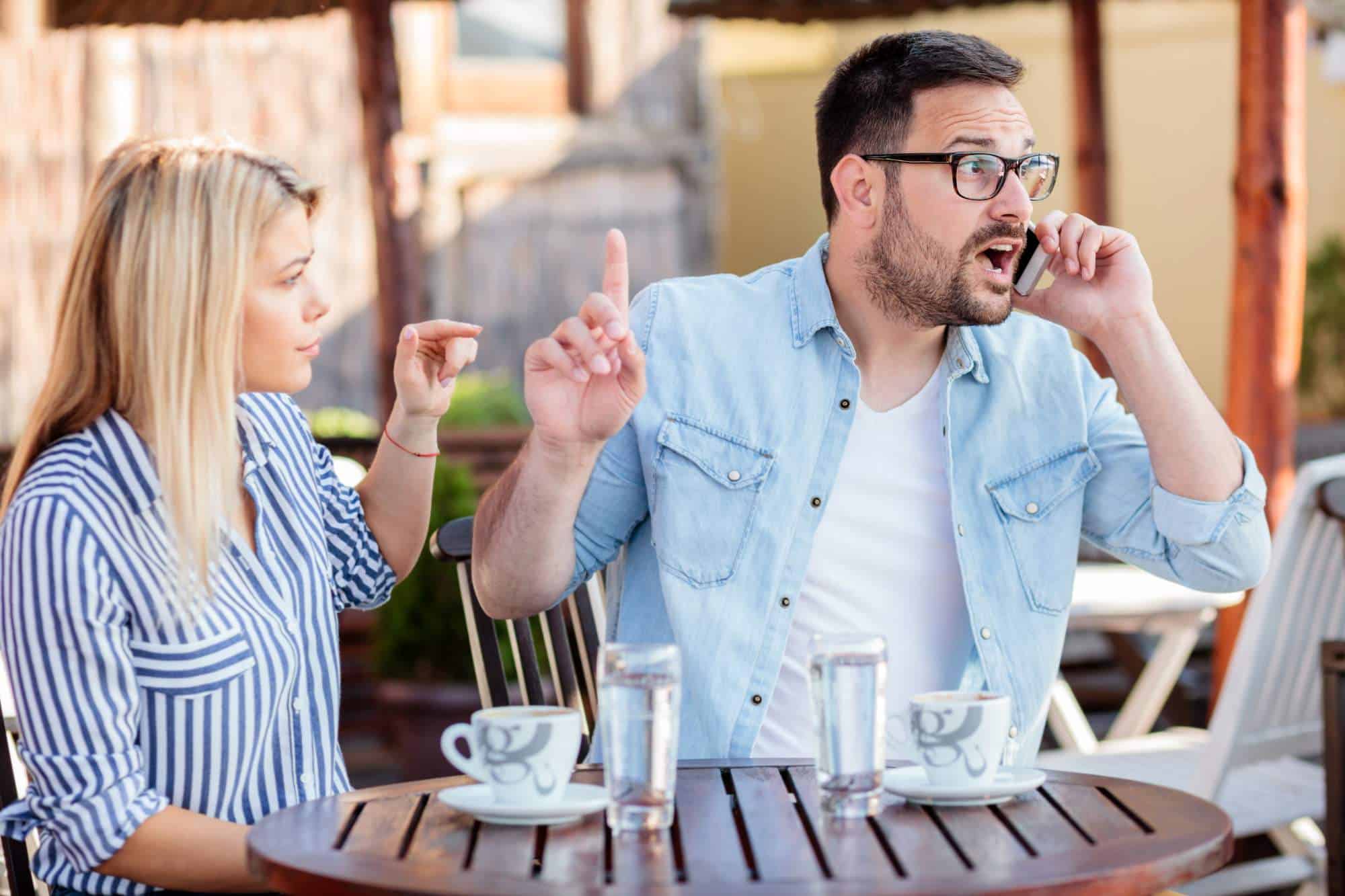Man ignoring his partner while on the phone with someone else, sending mixed signals and relationship doubts about the seriousness of their relationship.