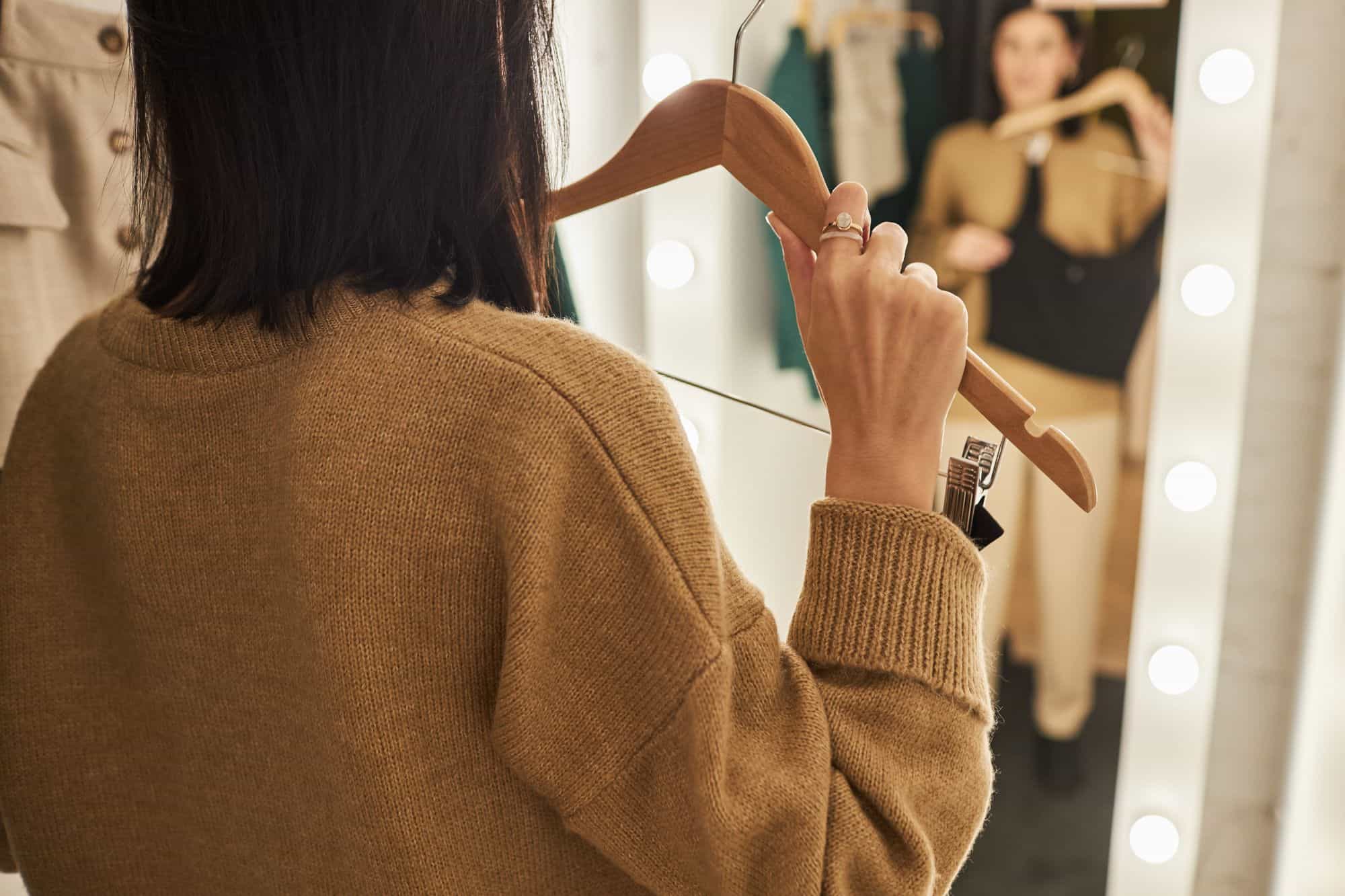 Woman standing in front of a mirror holding up tops while trying to decide what to wear on her first date.