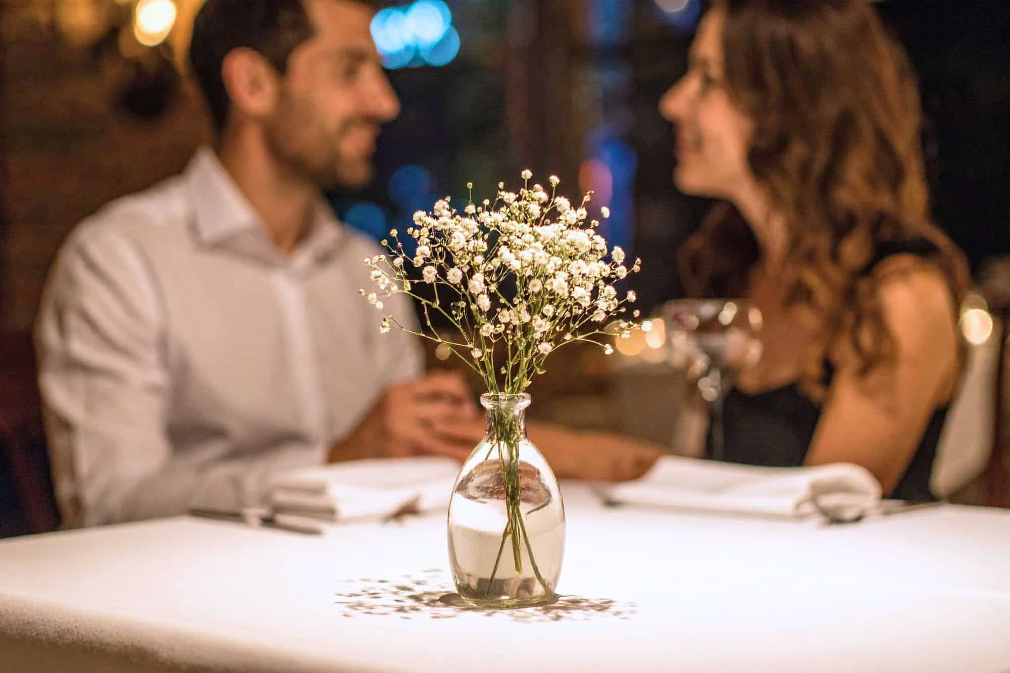 A man and woman who recently met through strategic dating sitting at a table with flowers, smiling at each other as they enjoy their dinner.