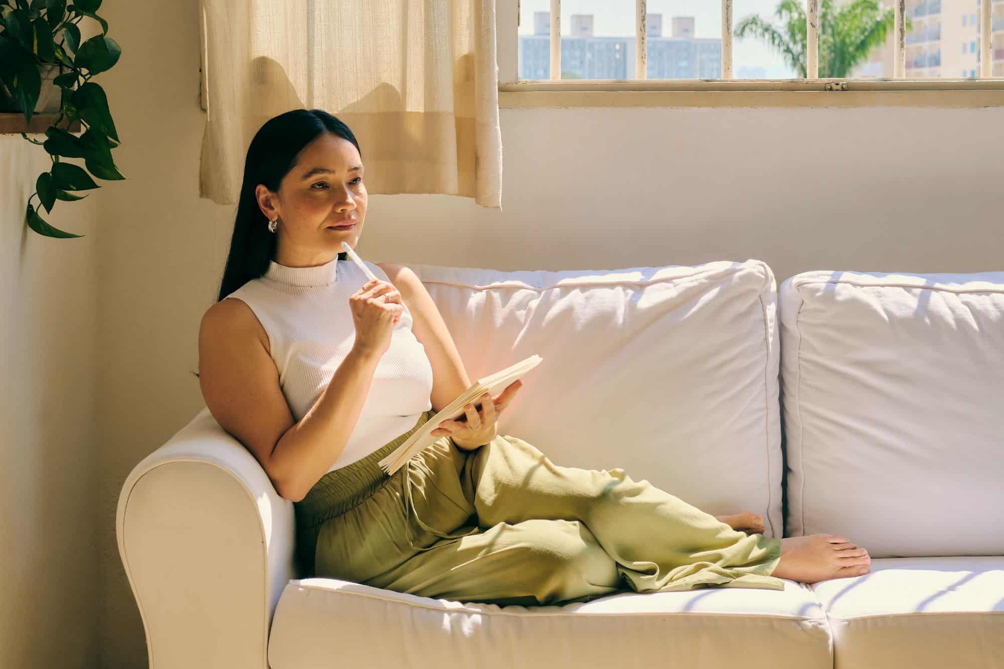 A woman sitting on her couch with a notebook and her pen to her lips, considering if she is truly prepared for love.