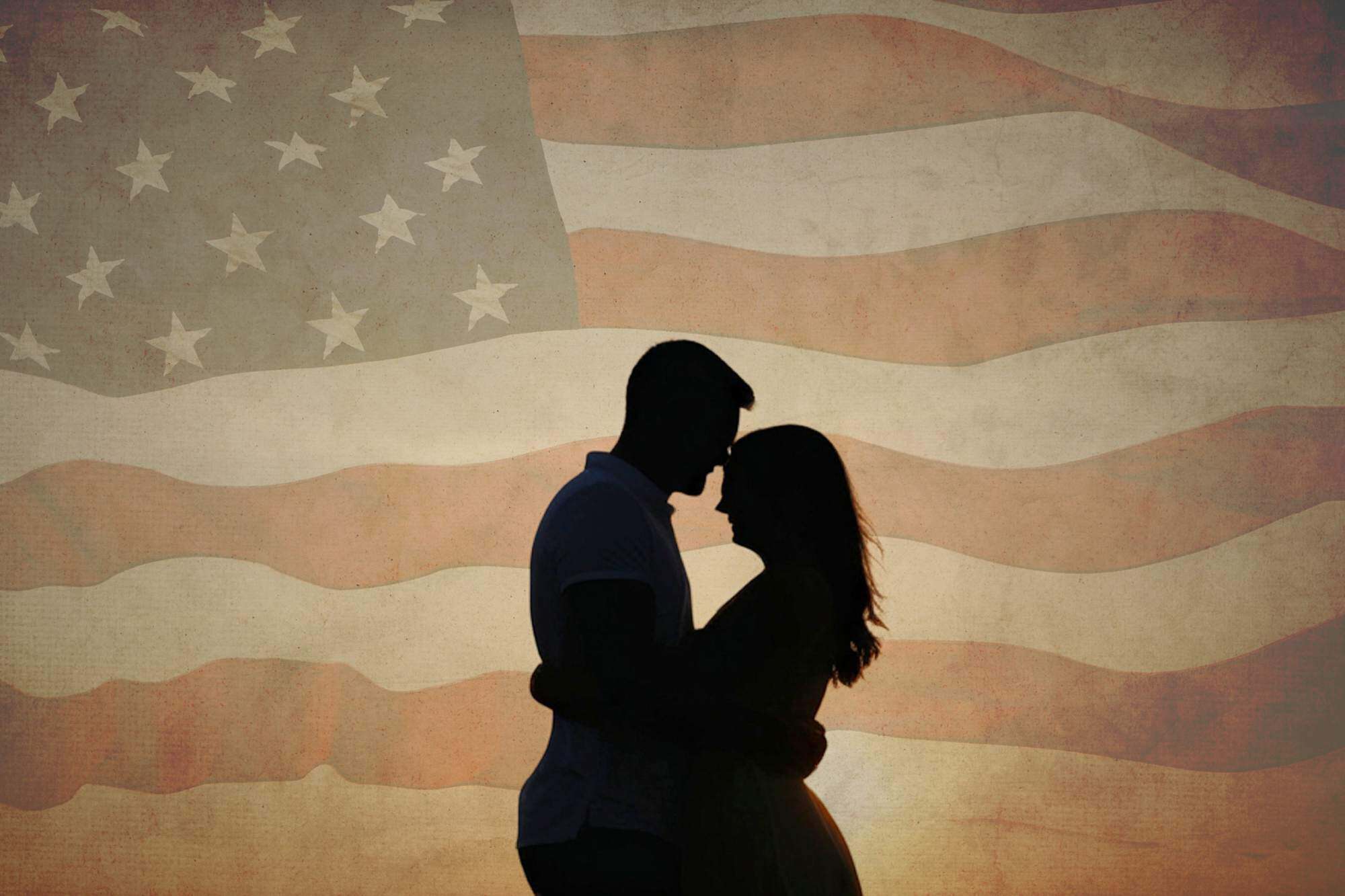 Silhouette of a couple in love in front of a faded American flag celebrating Independence Day.