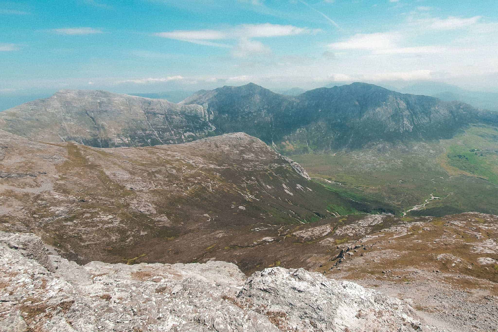 A scenic view of a mountain range with green valleys and rocky peaks, taken from the Benlettery hike under a clear sky.