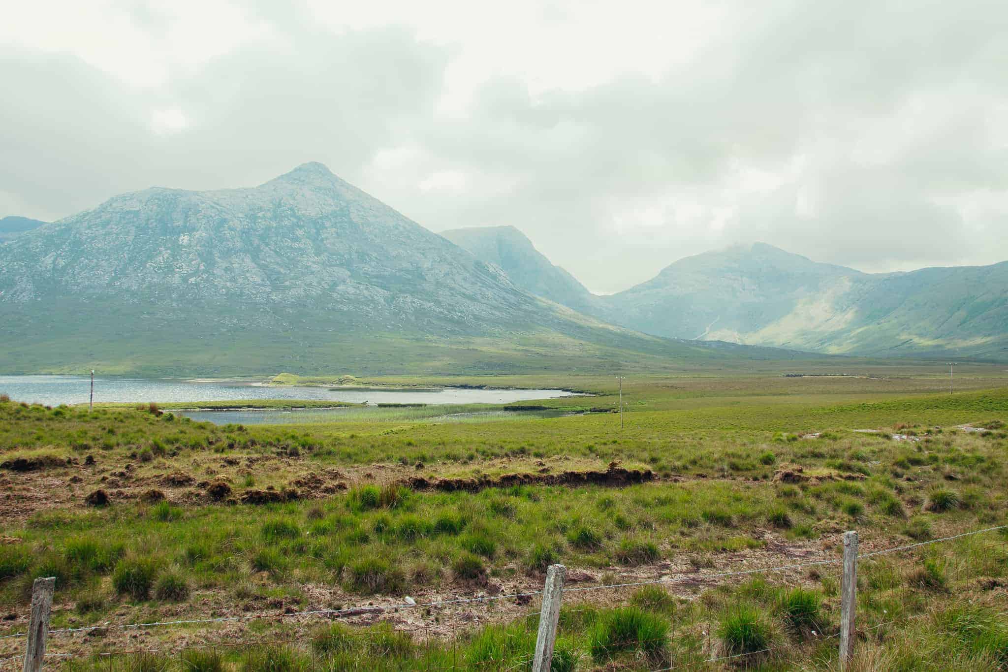 The lush, green expanse of Connemara National Park in Ireland, with a rugged mountain rising prominently in the background under a partly cloudy sky.