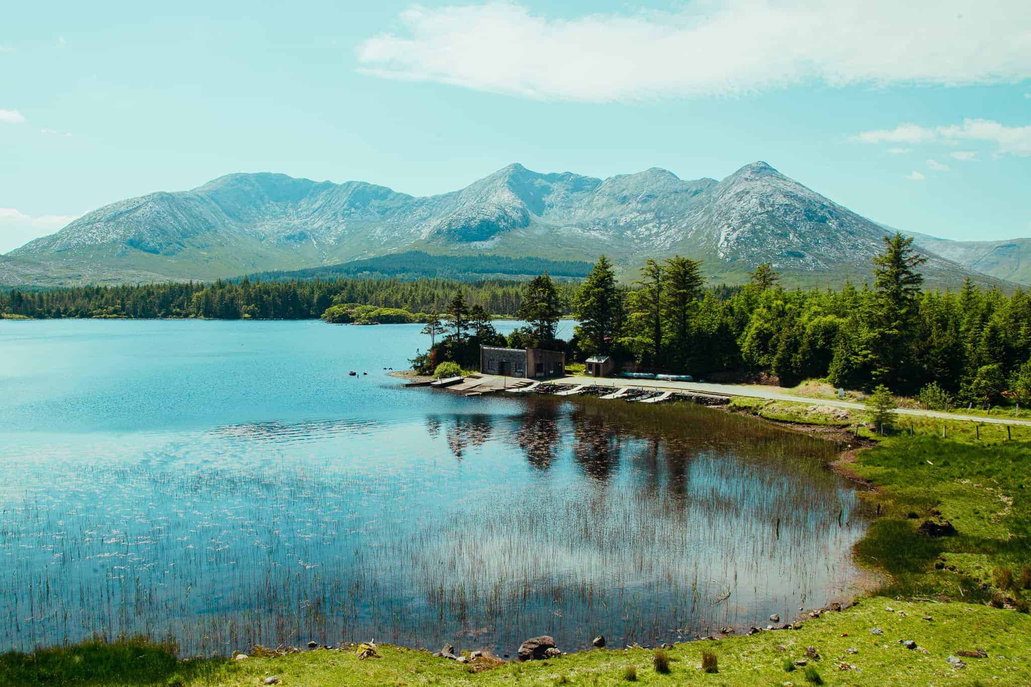 A picturesque view of Lough Inagh with clear blue water, surrounded by mountains and forests.
