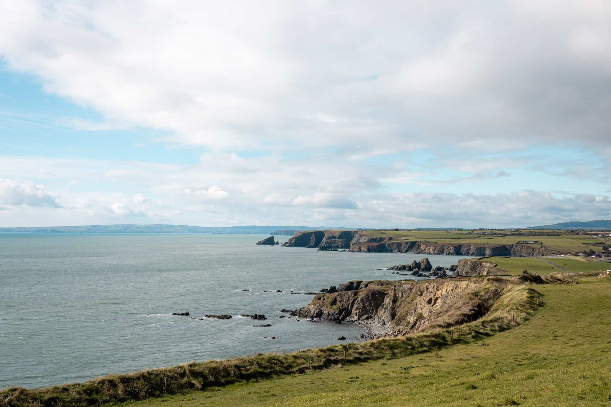 A wide view of the Irish coastline, with cliffs extending into the distance and the ocean glistening under a sunny sky.