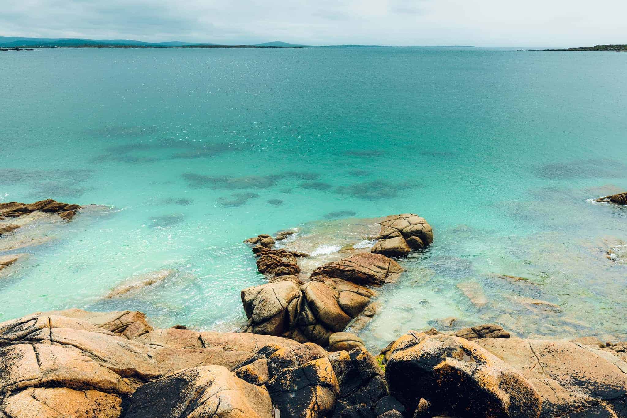 View from above of clear turquoise sea meeting rugged rock formations along Connemara’s coastline.