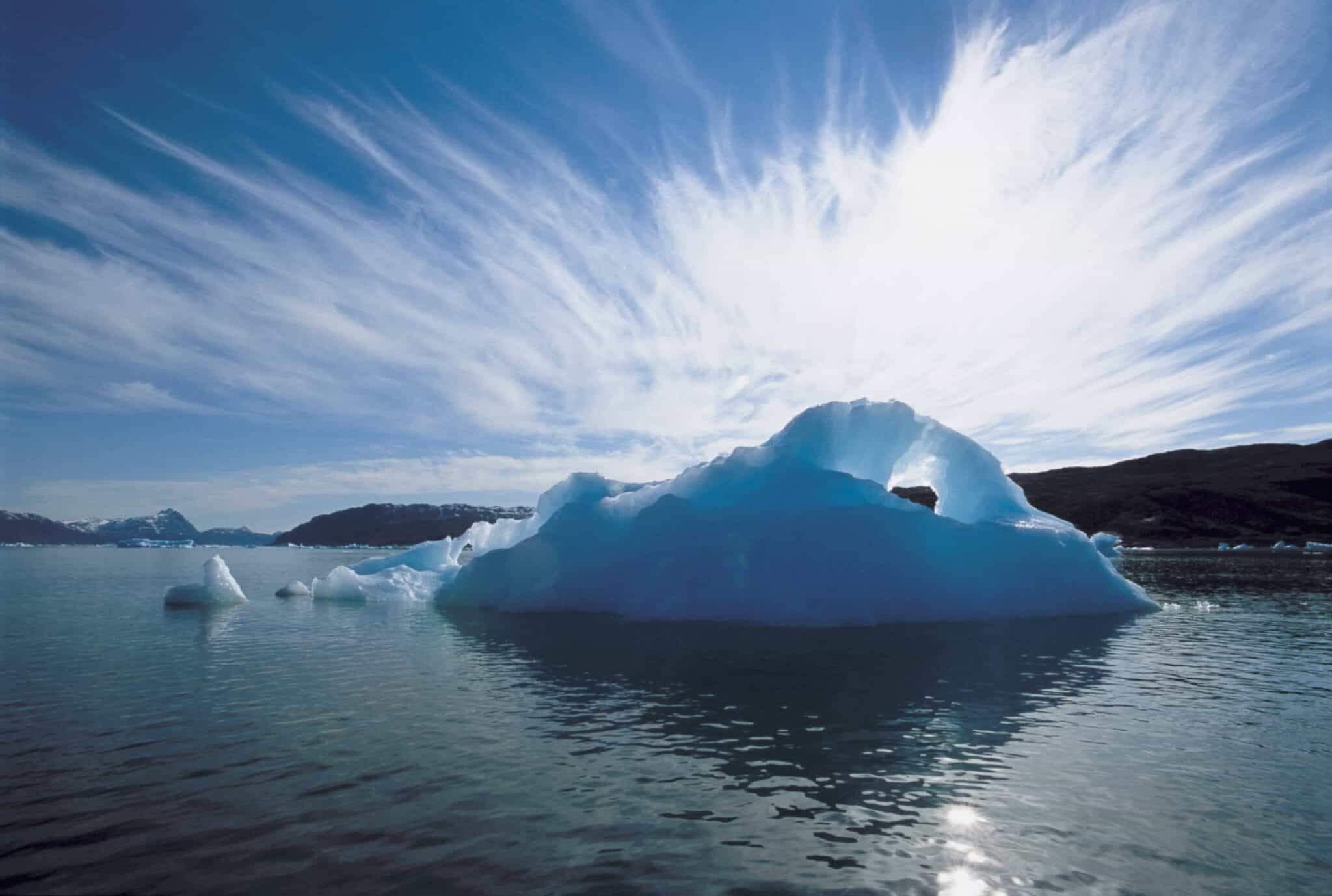 A large iceberg floats in calm water under a sky with streaked clouds, reminiscent of the serene landscapes of Lapland.