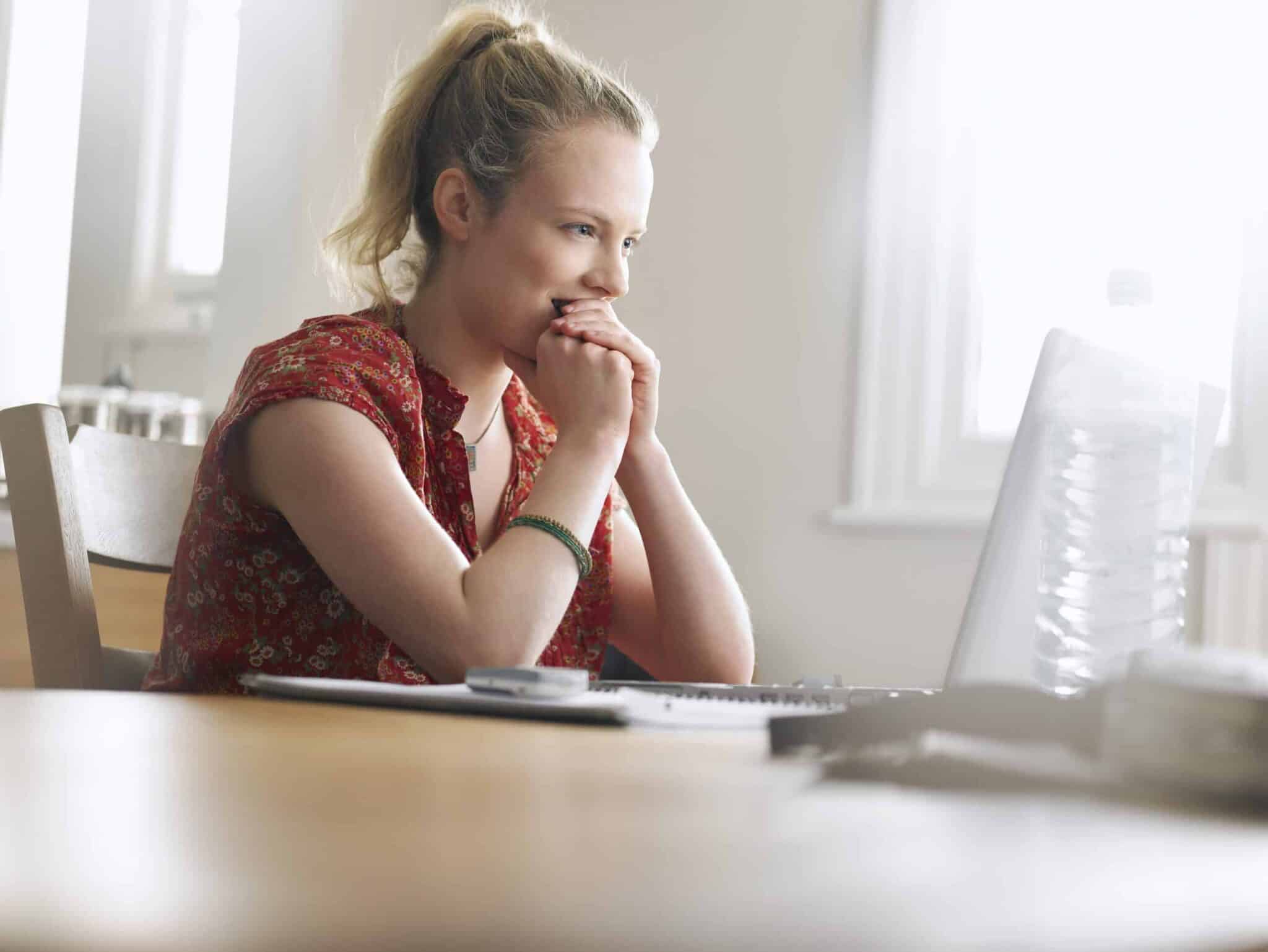 Woman looking excitedly at screen with hands clasped at her mouth