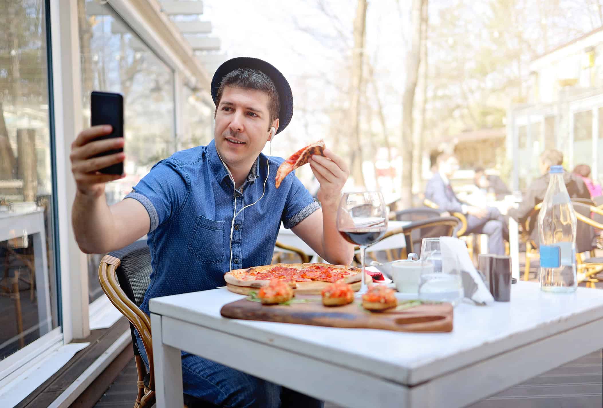 Man eating a pizza alone and taking a selfie.