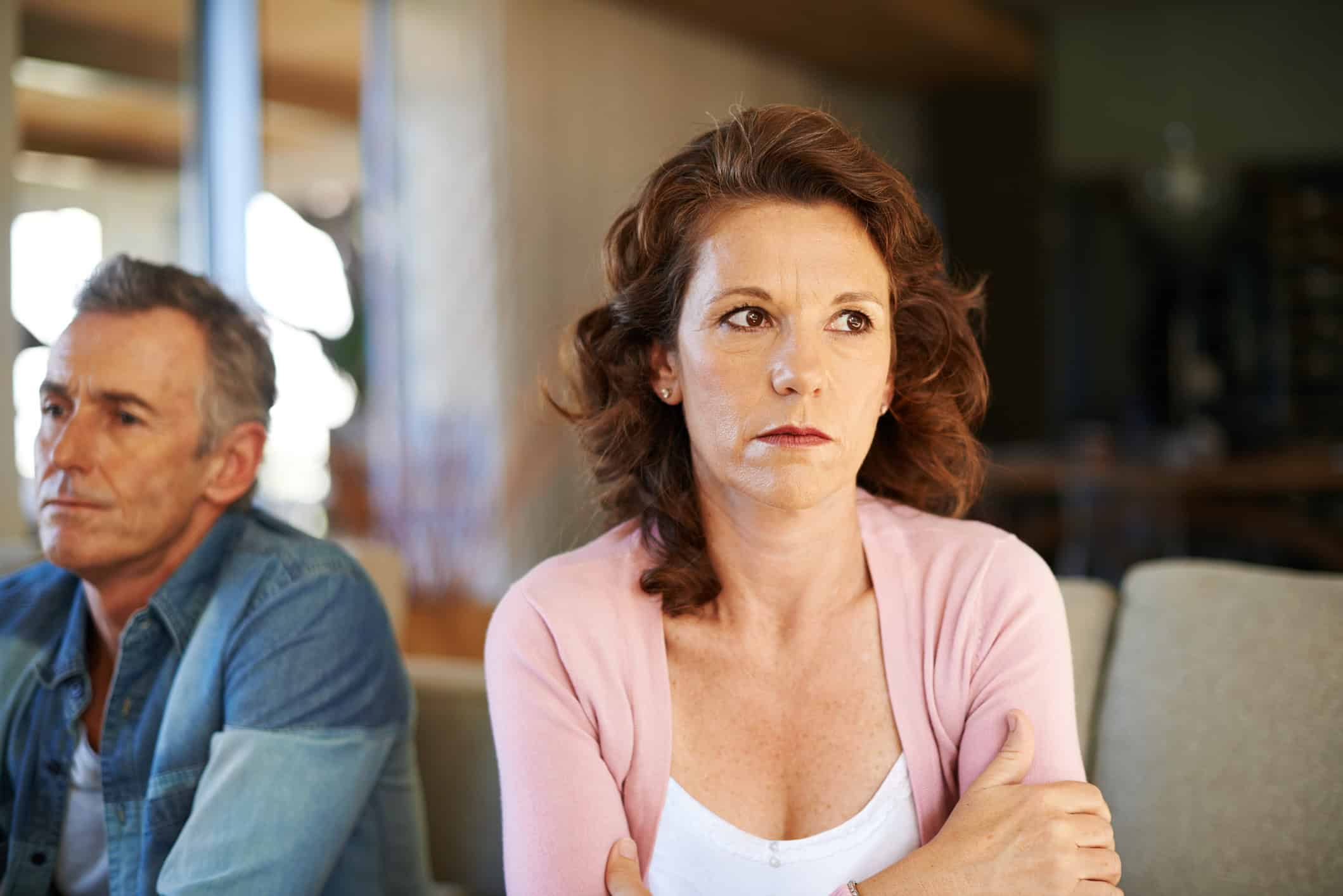 A concerned woman considering why her relationship doesn't feel right. She is looking away and sitting with her back to her uninterested-looking partner.