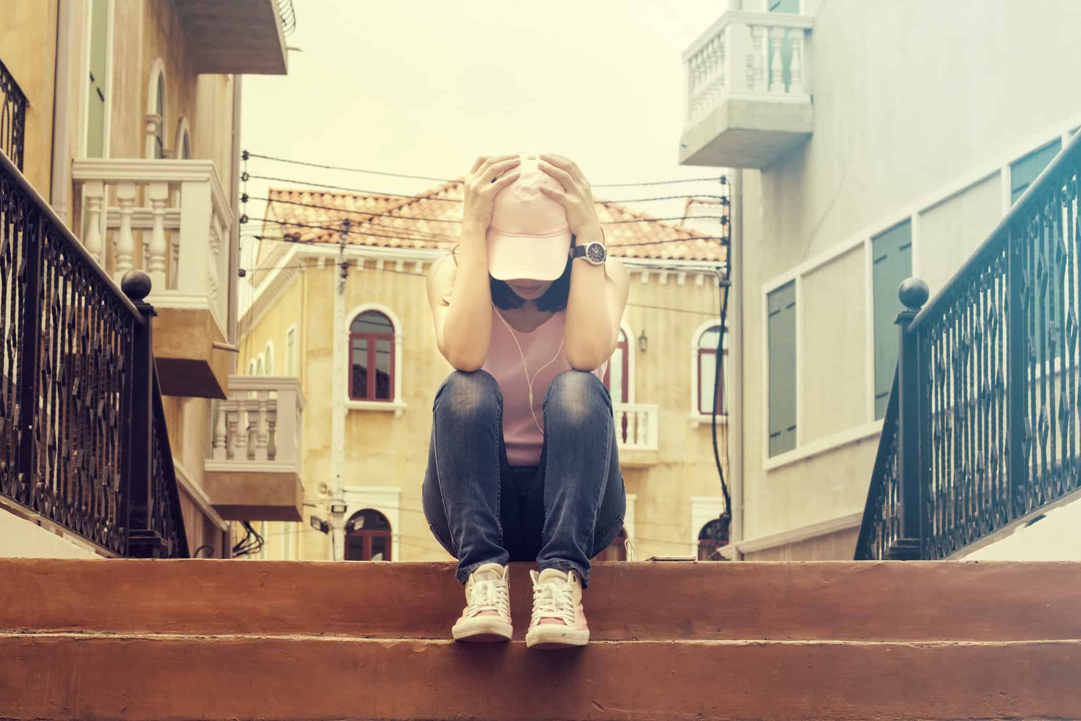 Pretty woman who is frustrated with matchmaker services/companies, sits on steps in the middle of the city with her head in her hands.