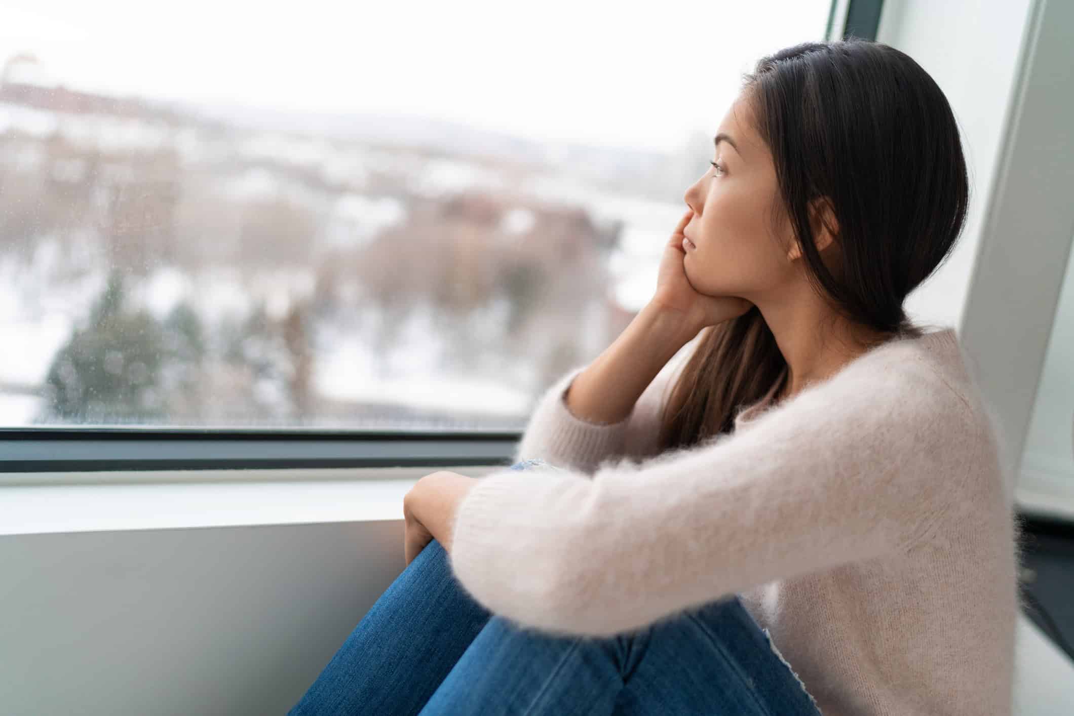 Woman looking out a window wondering when she'll find a love to last.