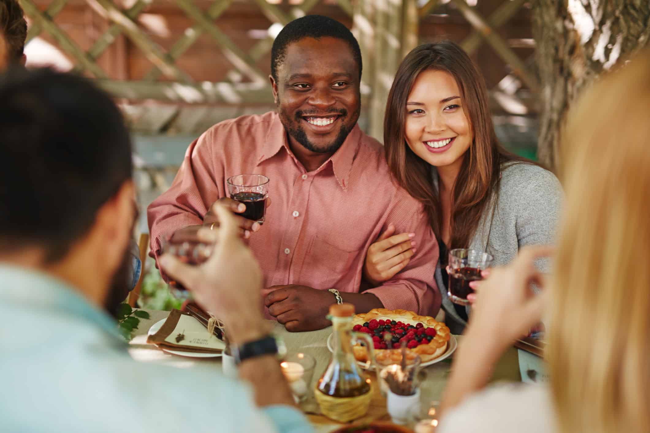 Multiracial couple enjoying a holiday dinner with friends and family after having must-have relationship conversations.