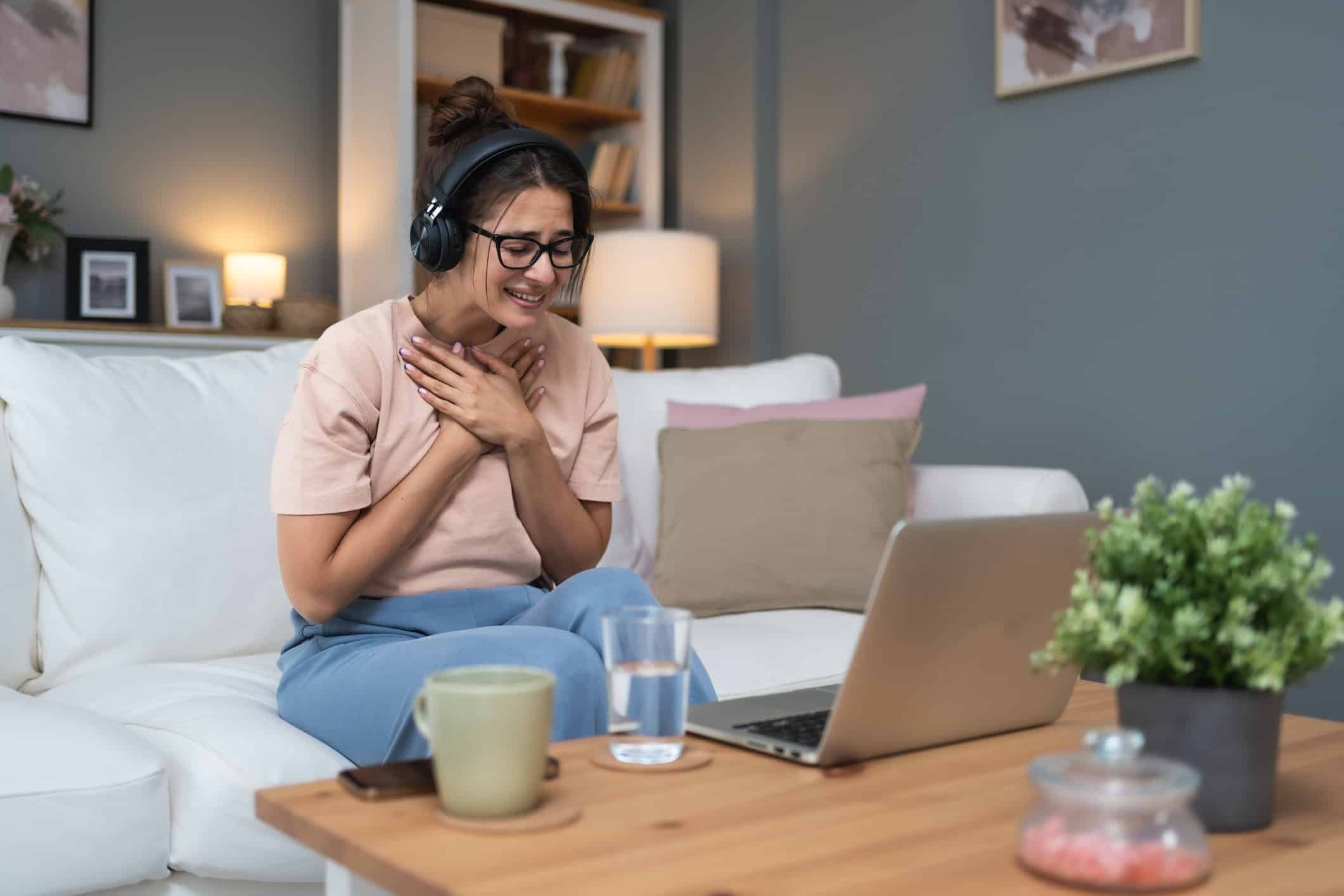 Woman sitting on couch clutching heart as she receives relationship coaching advice online to find lasting love.
