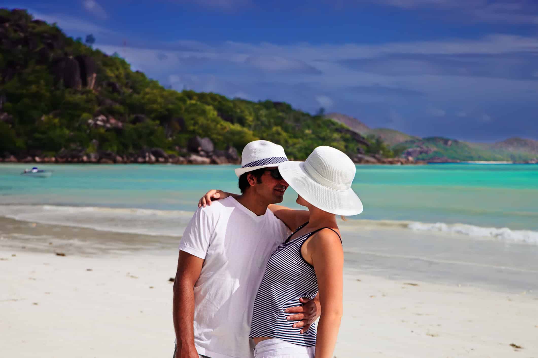 A happy couple on the beach who enjoy a realistic romance, embracing and leaning in for a kiss.