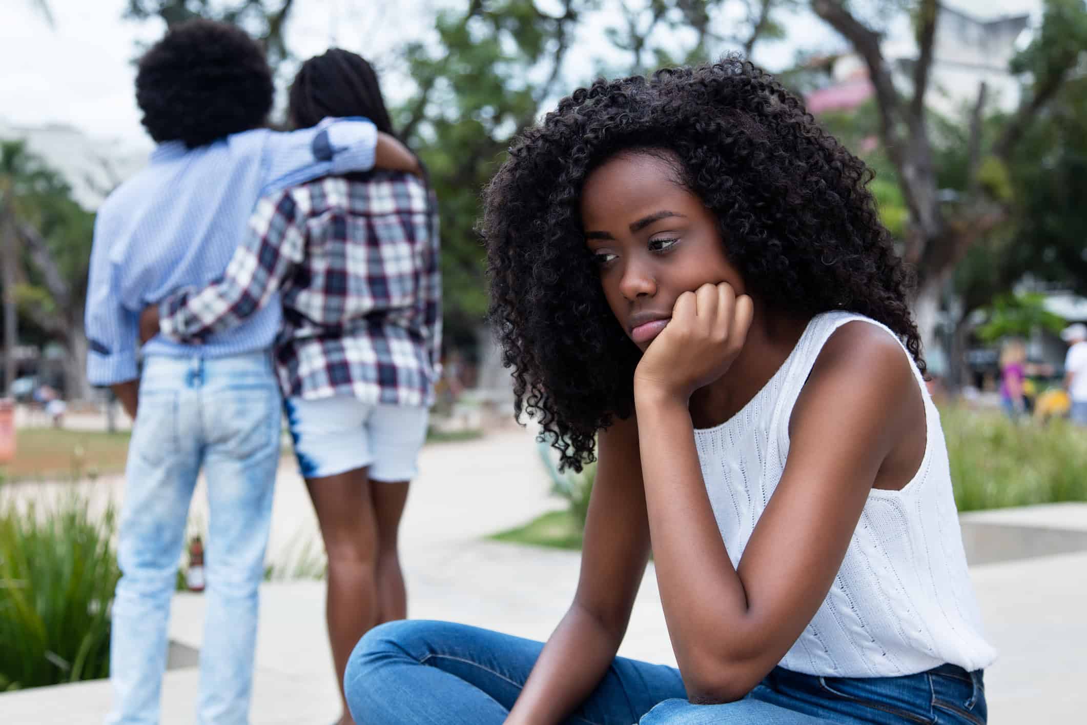 Woman looking dejected and wondering why she can't find love after a couple has walked past her.