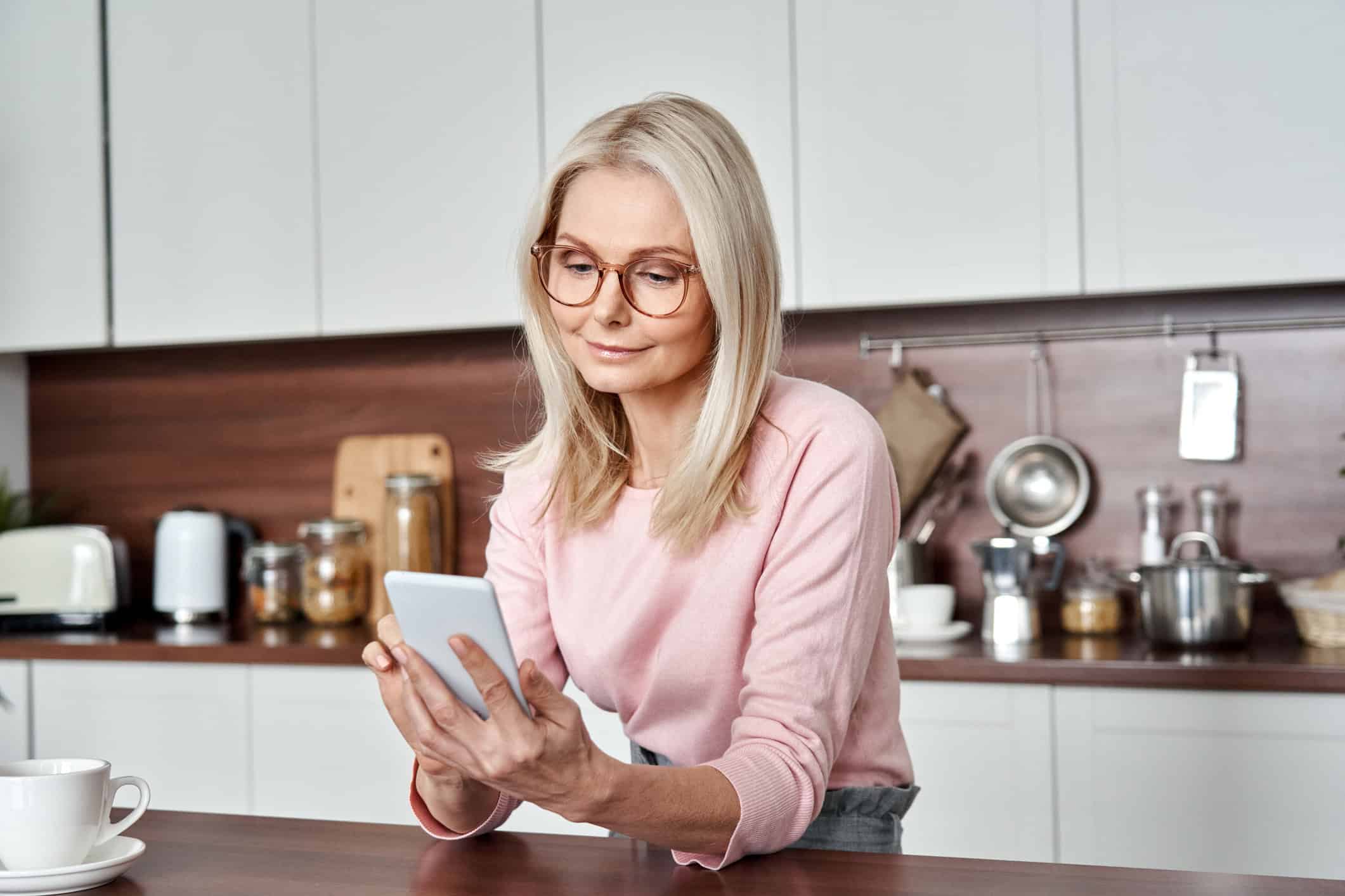 Woman sitting in her kitchen looking at her online dating app.