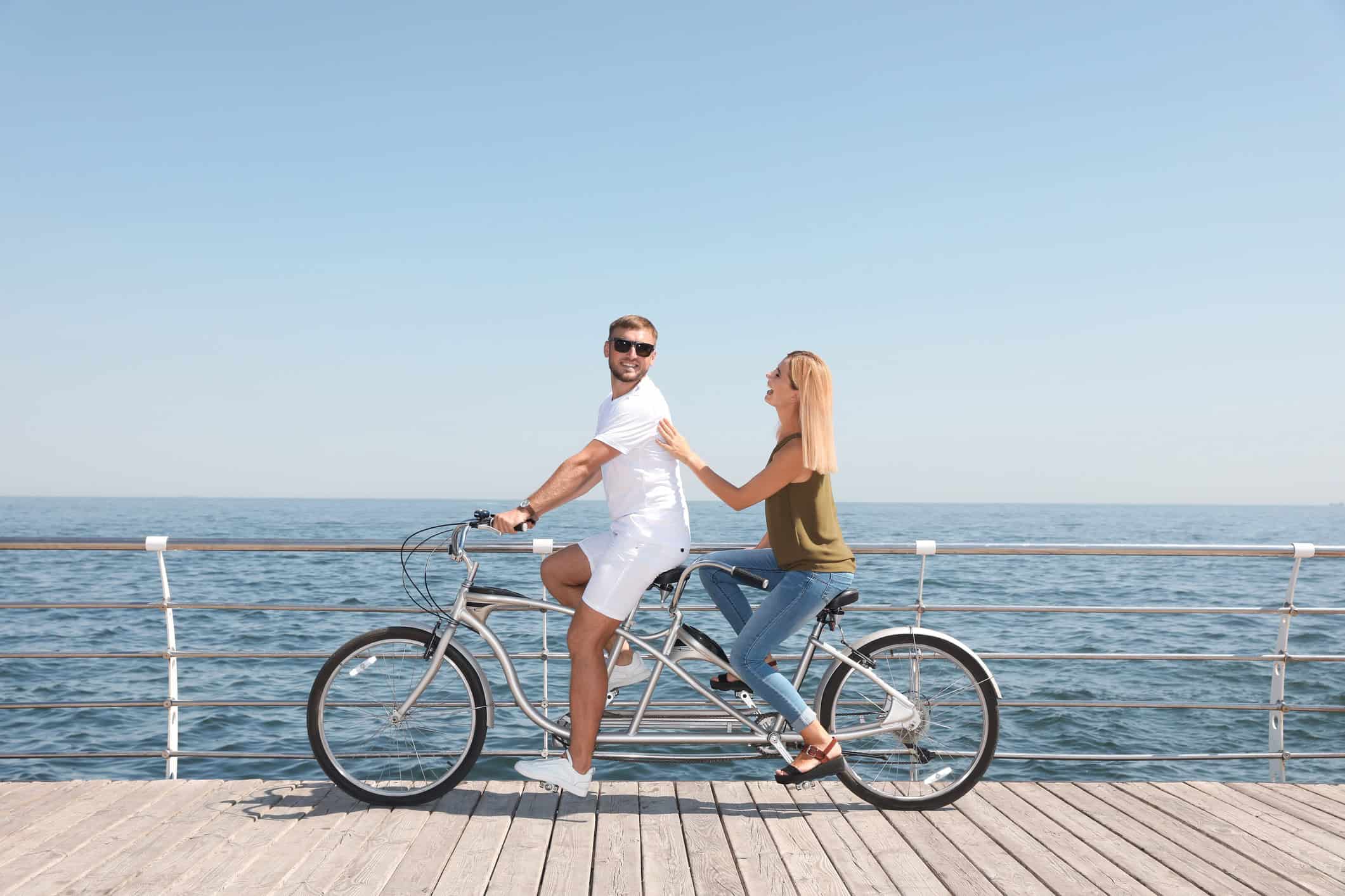 Couple riding a tandem bike on a boardwalk.