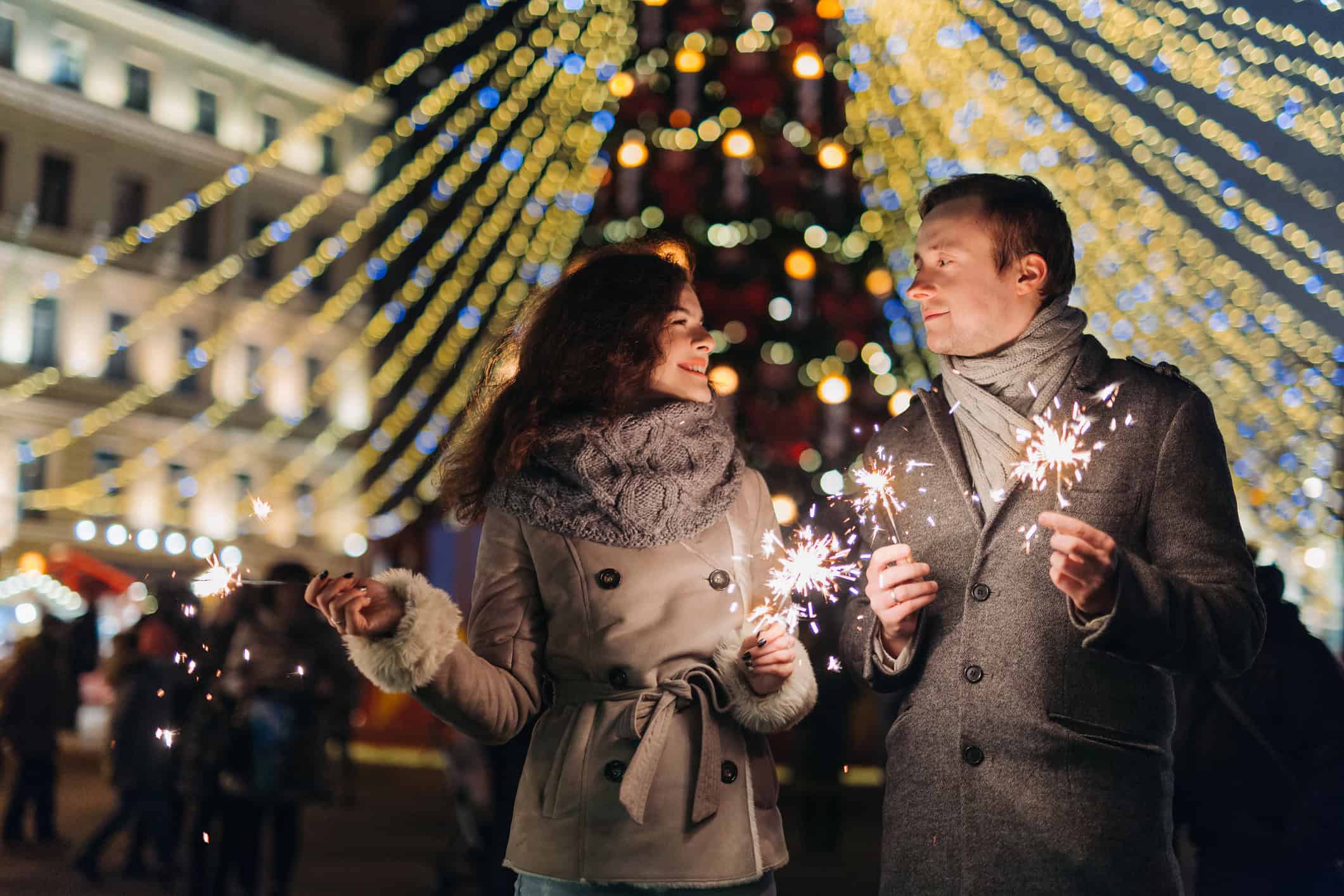 Couple bundled up outside and holding sparklers on New Years Eve as they look to attract love by turning over a new leaf in the new year.