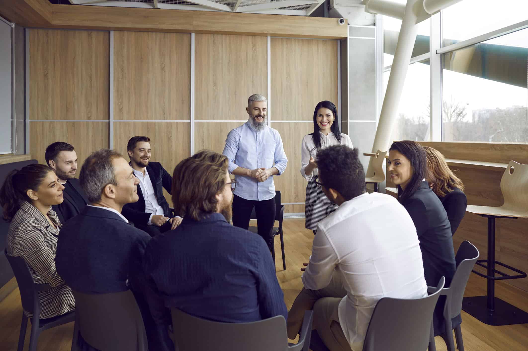 A group of professionally dressed Life and Relationship Coaches sitting in a circle, smiling and discussing training and ideas.