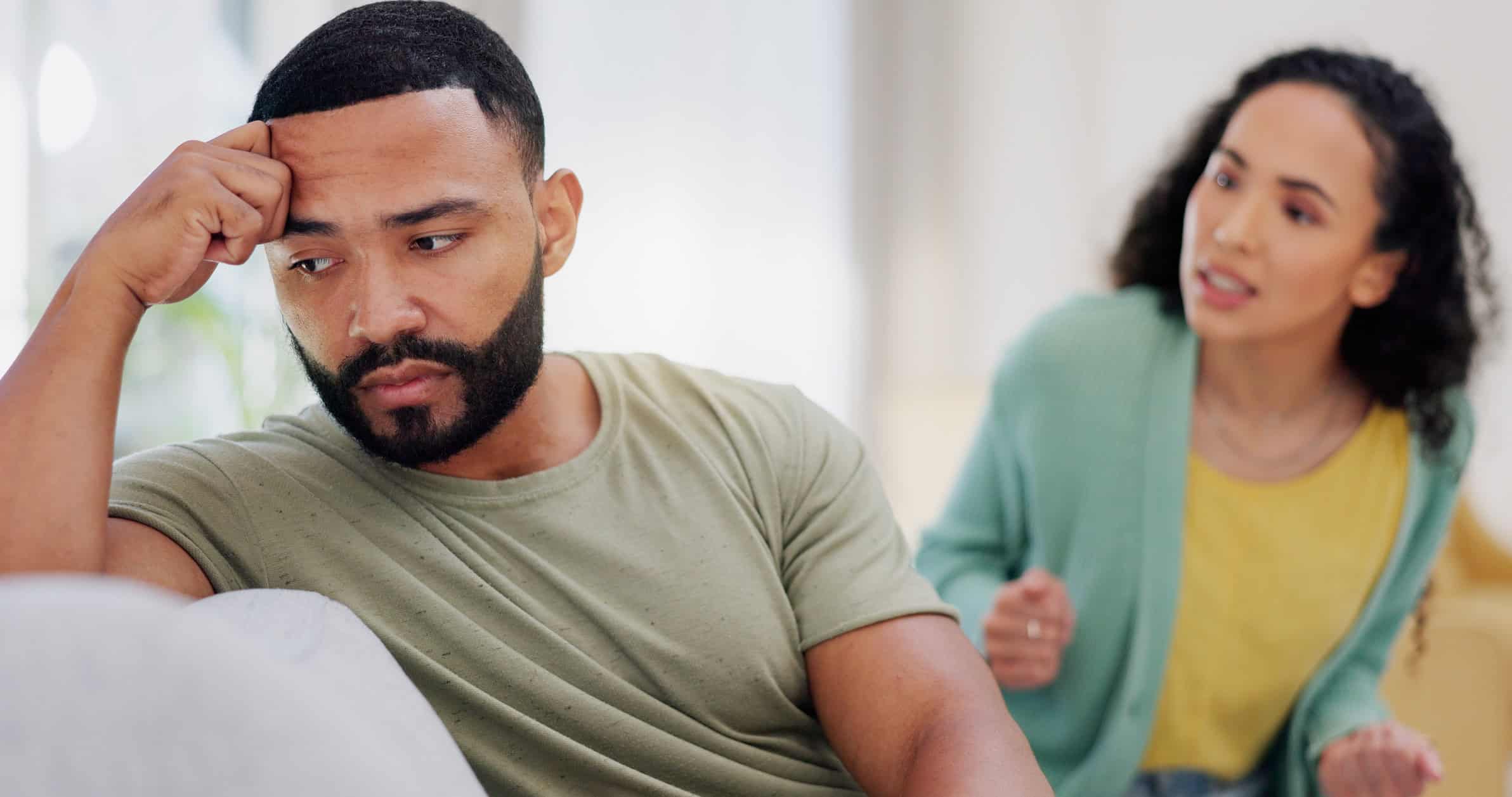 A frustrated man sitting on the couch has turned away from his angry girlfriend as the couple argues about breaking up.