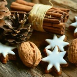 Sprigs of cinnamon, star-shaped cookies with white icing, walnuts, and pinecones arranged on rustic wooden surface for holiday or winter celebration.