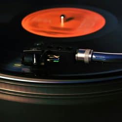 Turntable playing vinyl record with orange label, close-up of tonearm and stylus, music vinyl record player, analog audio equipment, musical entertainment, high-quality sound, retro music technology.