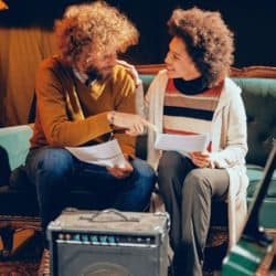 Professionals collaborating in a creative workspace discussing music production, with audio equipment, documents, and a cozy environment, emphasizing music industry, collaboration, and creative process.