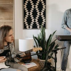 Teens practicing music at home, young musicians with electric guitar and keyboard, cozy indoor setting, creative music session, indoor rehearsal, musical instruments, home music studio, learning music, casual band practice, youthful musicians.